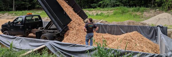 A woodchip bioreactor, under construction here in 2018 in the Town of Bolton, New York, removed 38% of cyanobacteria-causing nitrate from wastewater that flowed through it compared to zero removal of nitrate from the rest of the wastewater treatment plant’s effluent stream. Photo: Kathy Suozzo, P.E. Dump truck unloads woodchips into pit while a person watches